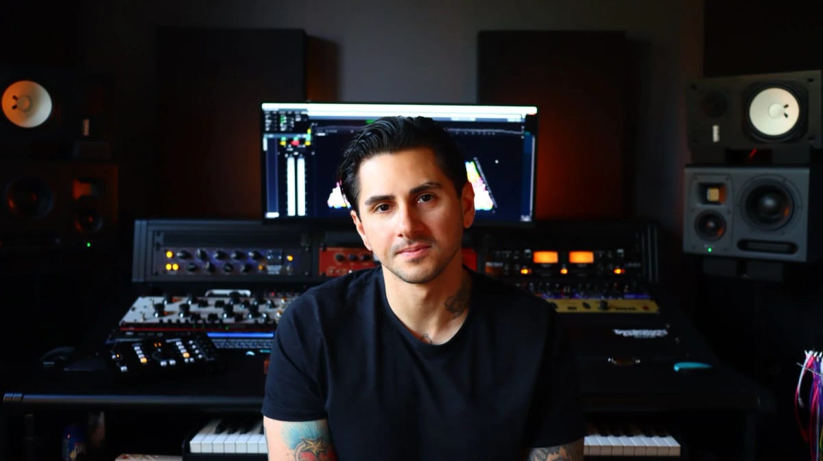 Seated at a mixing desk between studio monitors, racks of outboard gear and a screen