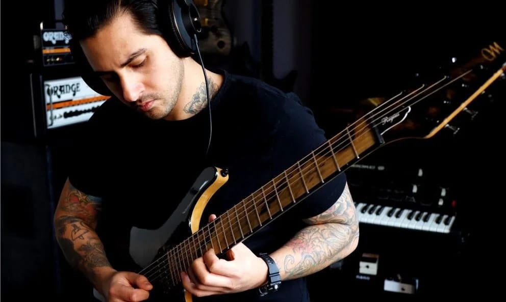 Edward Ray in headphones playing electric guitar beside an amp and keyboard in his studio